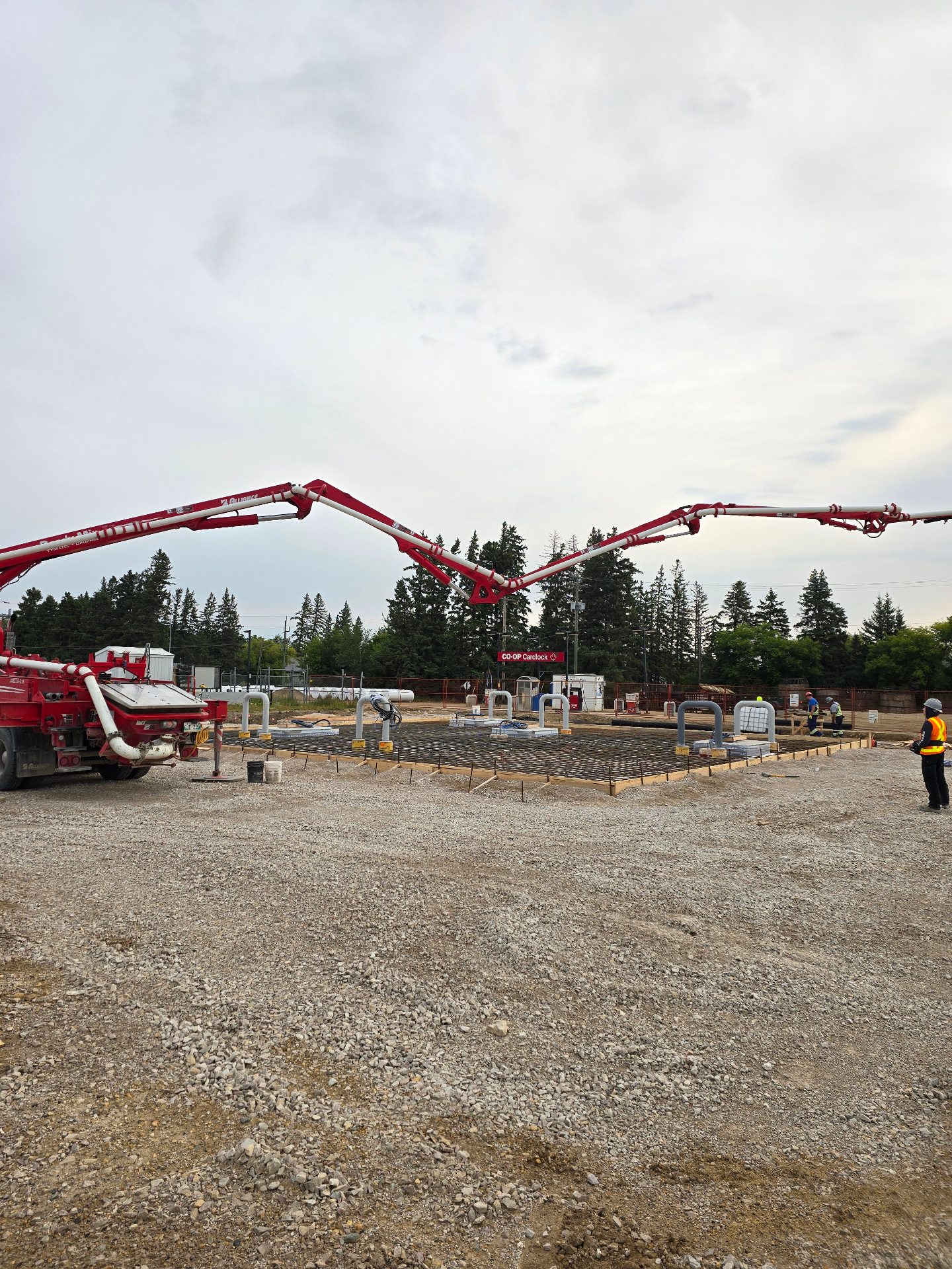Concrete boom pump placing rebar-reinforced fuel island slab at a Co-op cardlock in Manitoba